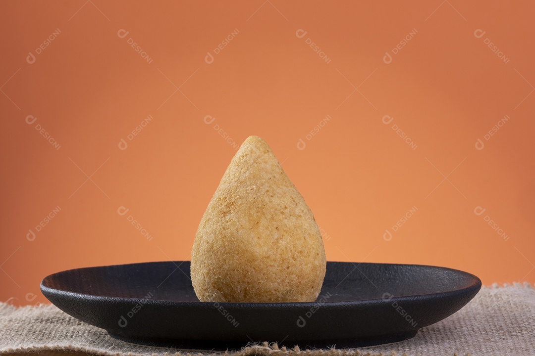 Coxinha em um prato preto com fundo laranja