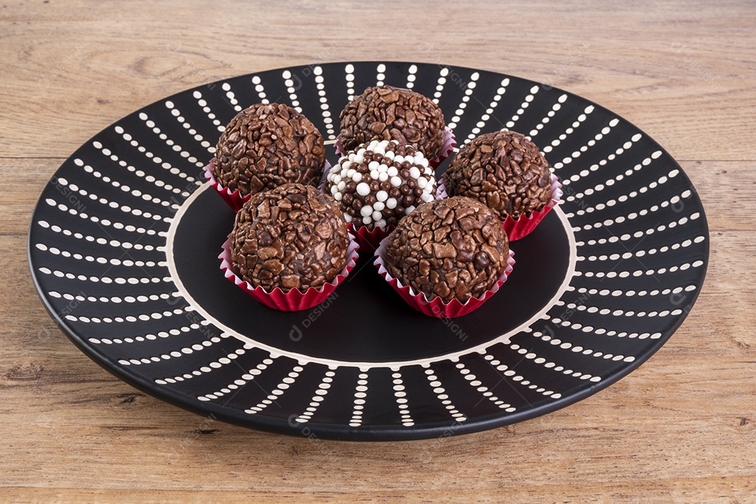 Brigadeiros em prato preto na mesa de madeira