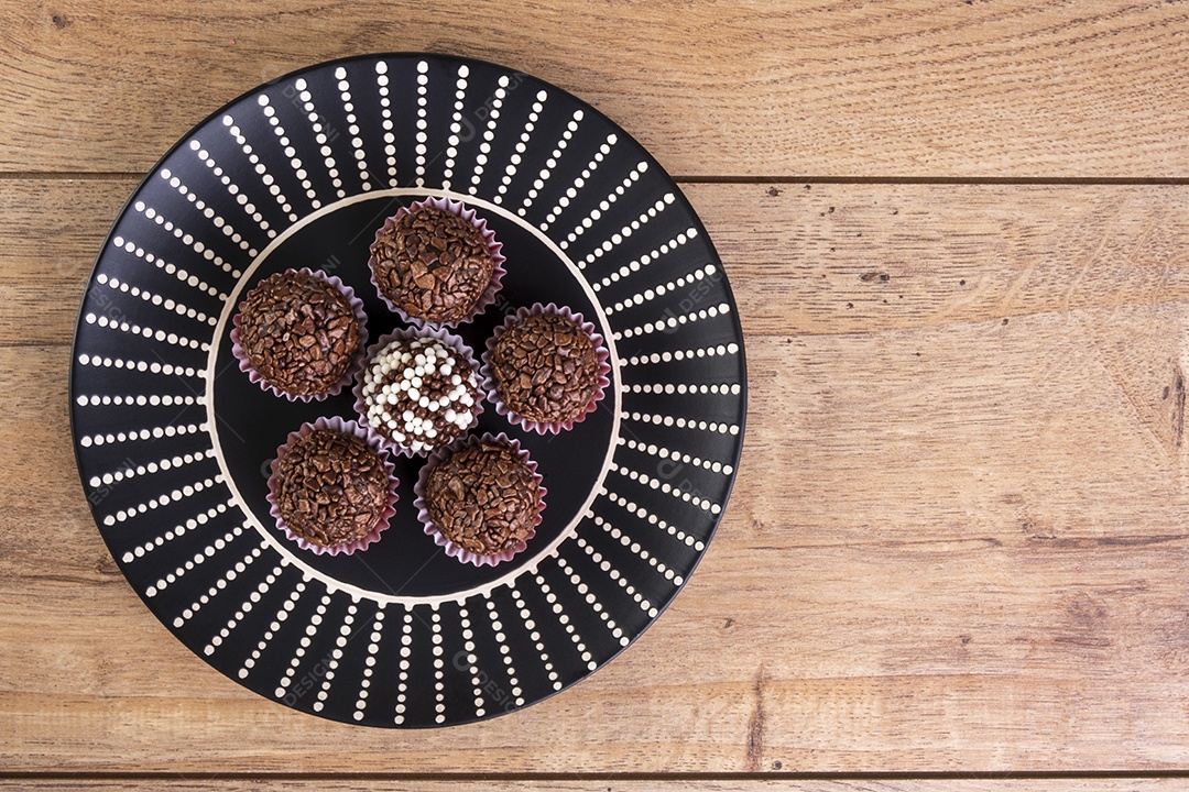 Brigadeiros em prato preto na mesa de madeira