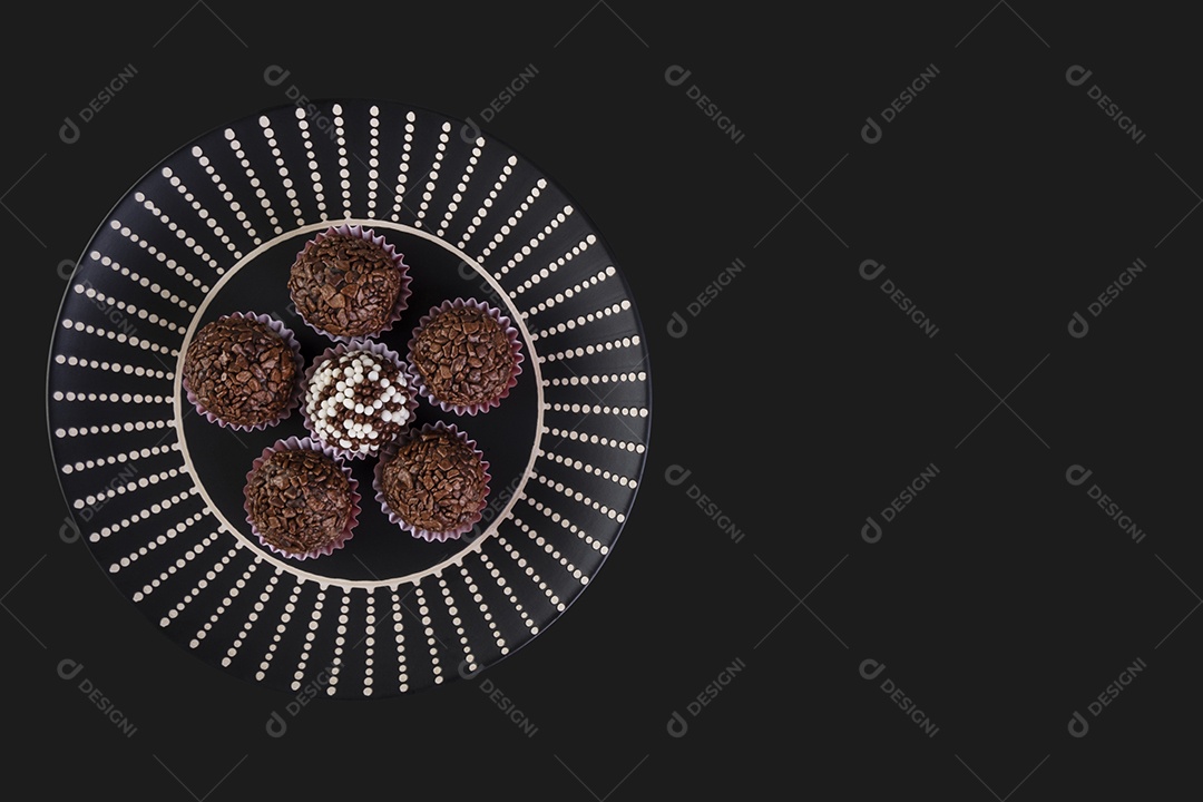 Brigadeiros em chapa preta com decoração branca sobre fundo preto.