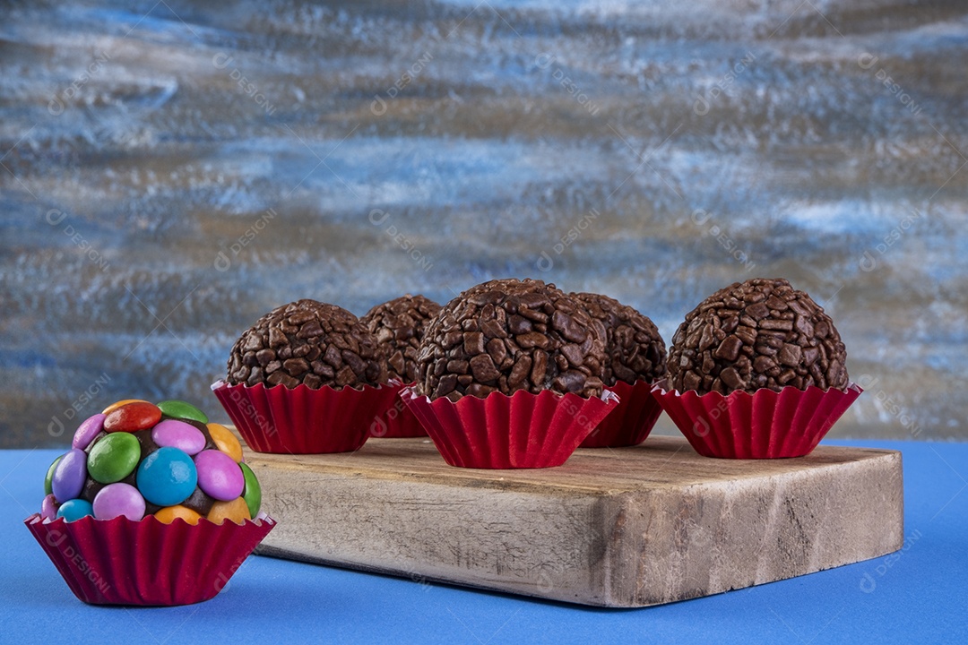 Brigadeiros variados em tábua de madeira com fundo multicolorido