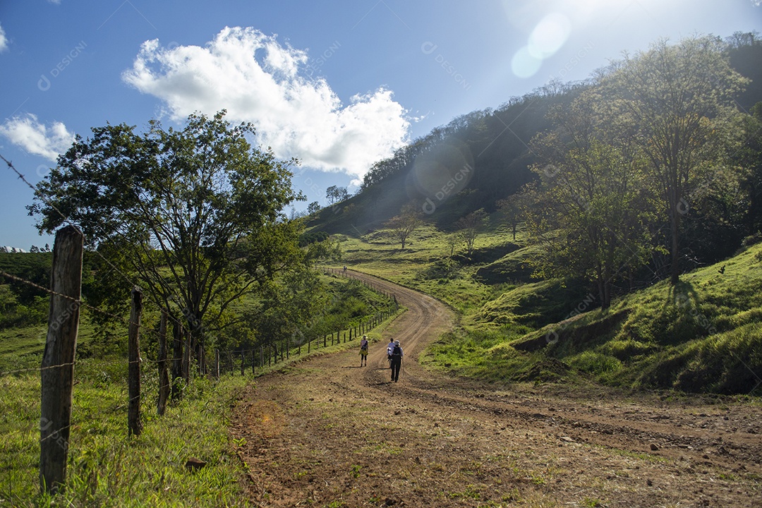 Pessoas andando em estrada de terra com montanhas ao fundo