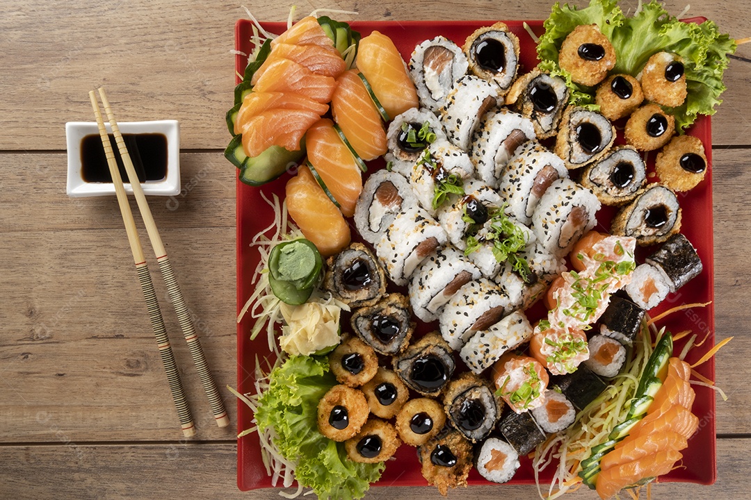Vários sushi no prato vermelho na mesa de madeira.
