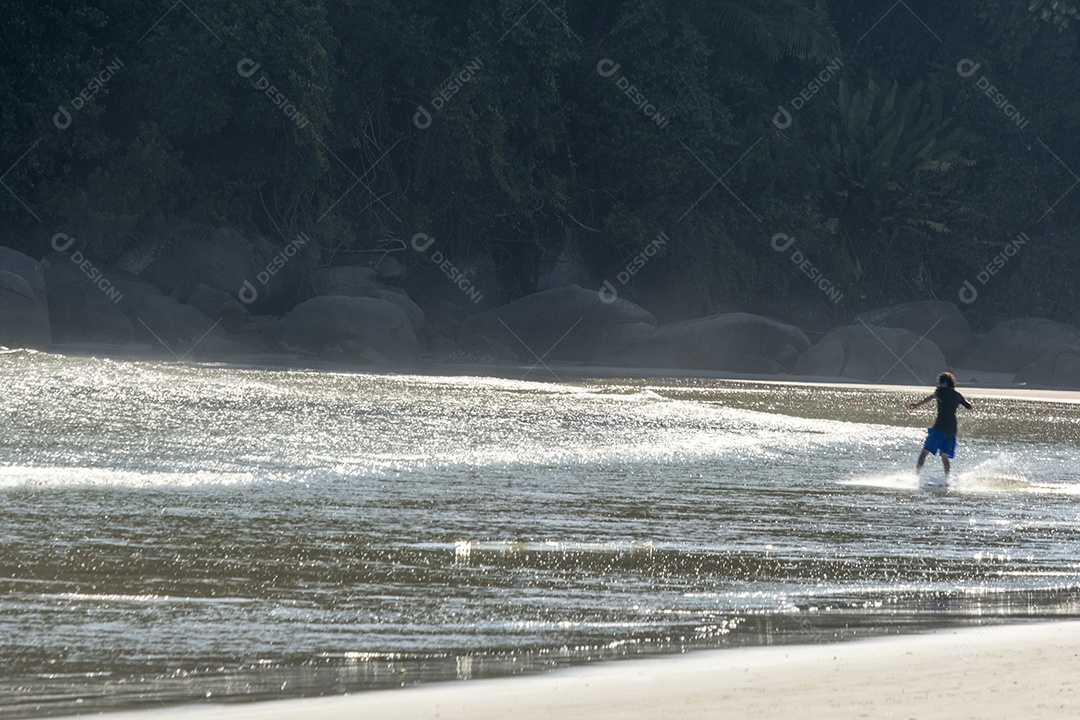 Menino brincando na água da praia no final da tarde.