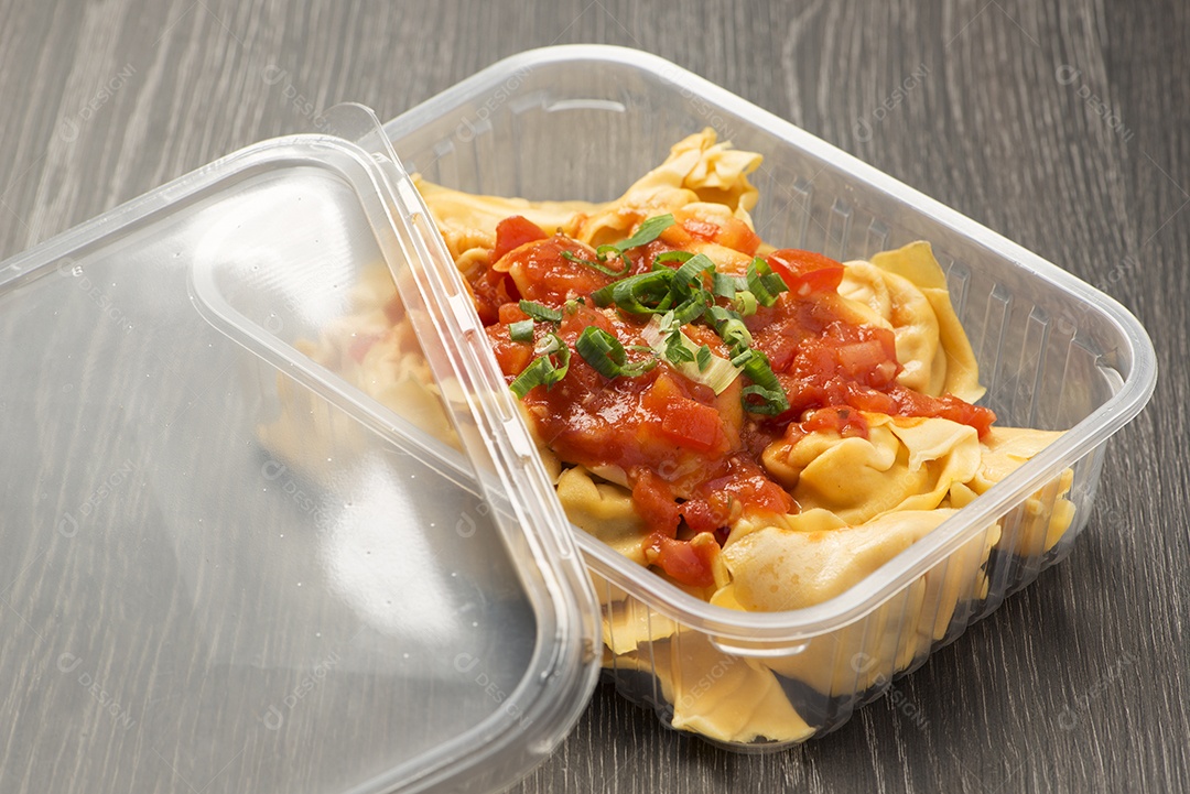 Lancheira plástica com ravióli e molho de tomate polvilhado com cebolinha.