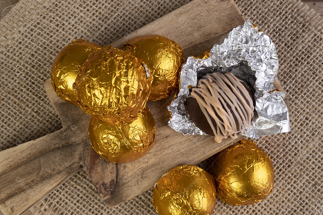 Trufas de chocolate embrulhadas em papel laminado na tábua de madeira