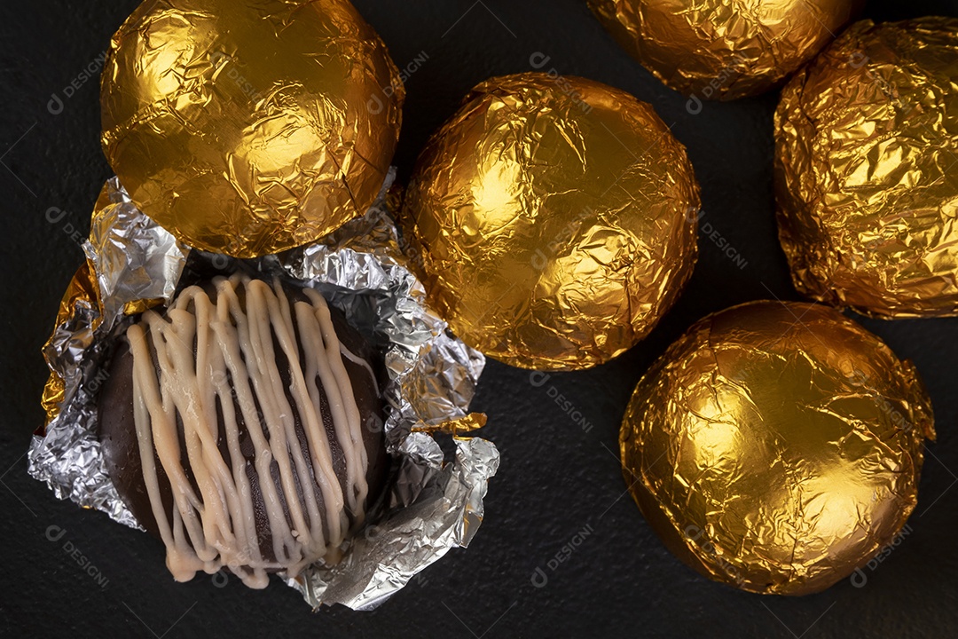 Trufas de chocolate embrulhadas em folha de ouro na chapa preta