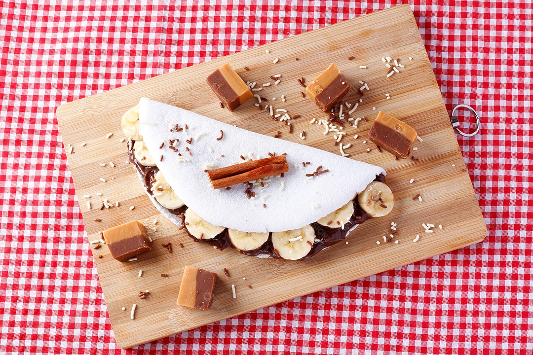 tapioca caseira ou beiju recheado com banana e chocolate na chapa branca sobre mesa de madeira rústica. vista do topo