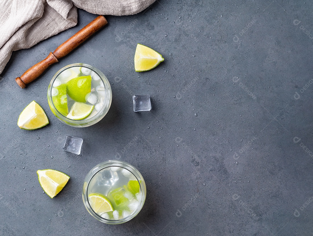 Caipirinha de limão brasileiro em copos com gelo e fatias de frutas sobre fundo de pedra.