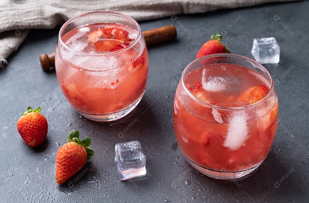 Caipirinha de morango brasileira em copos com gelo e frutas sobre fundo de pedra.