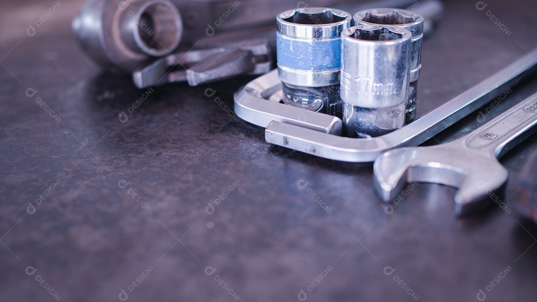 Ferramentas manuais consistindo de chaves, alicates, chaves de soquete, dispostas em fundo de chapa de aço antigo.