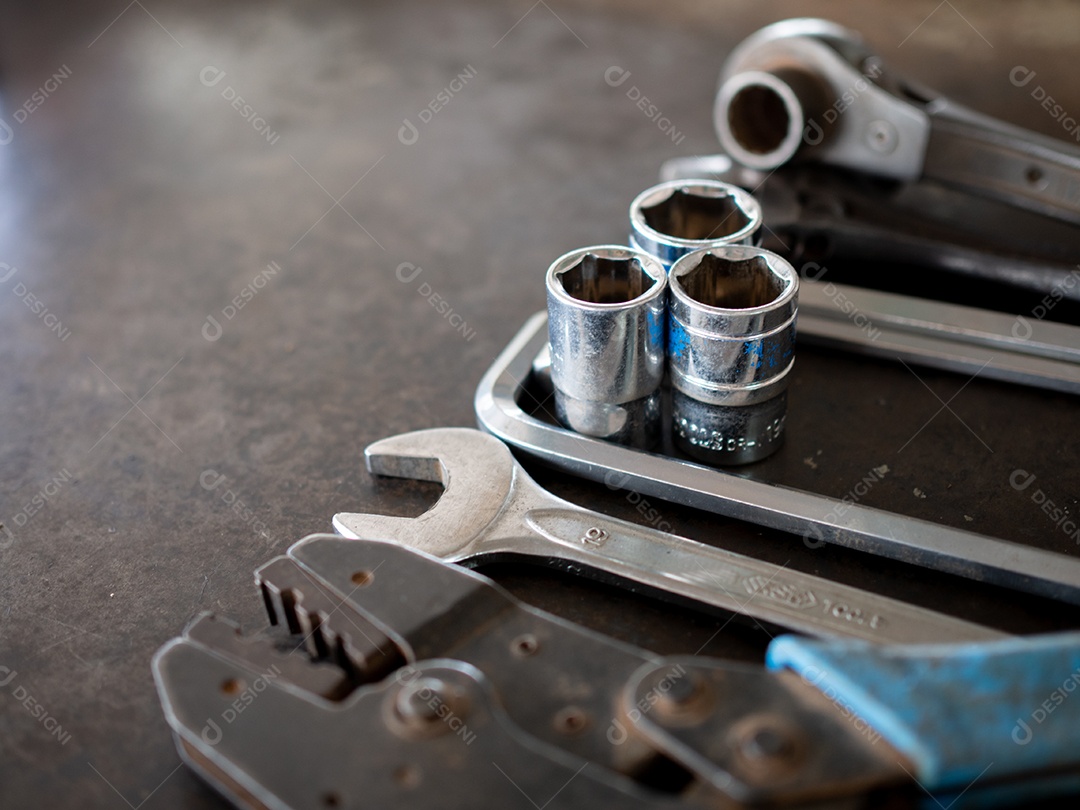 Ferramentas manuais consistindo de chaves, alicates, chaves de soquete, dispostas em fundo de chapa de aço antigo.