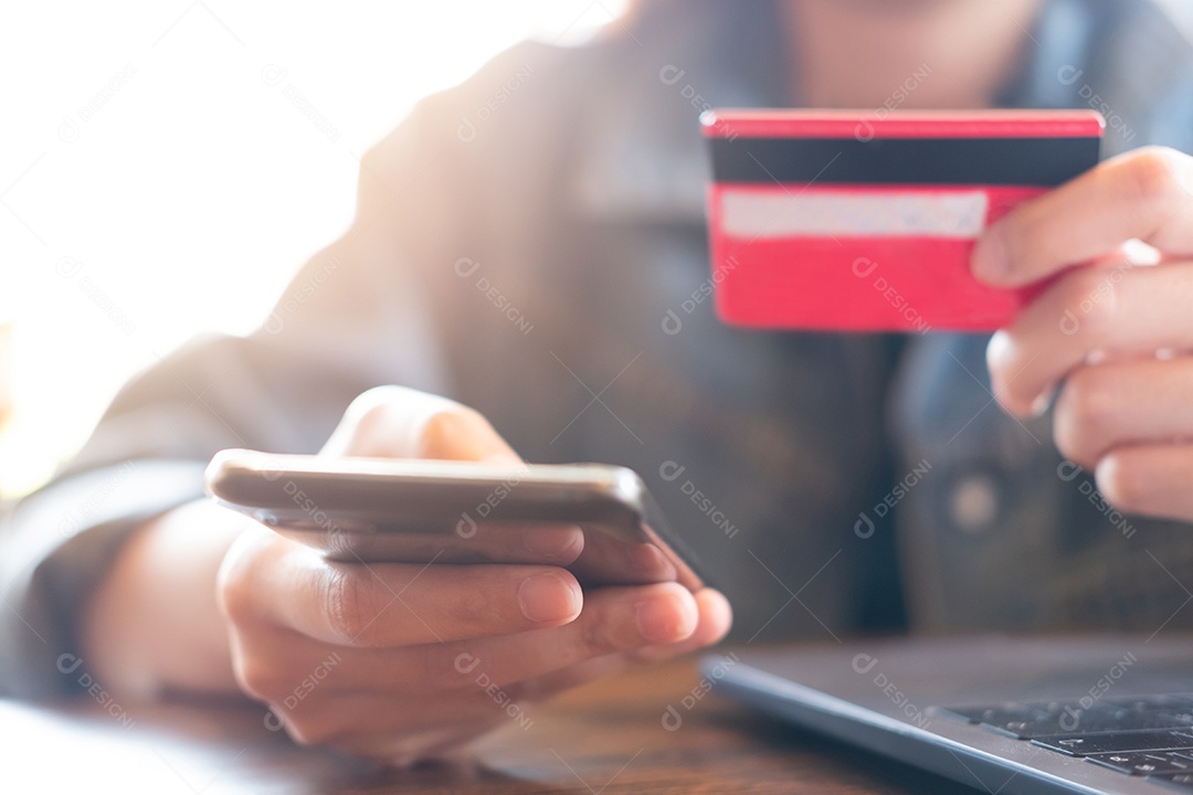 Mãos segurando um cartão de crédito e usando um laptop.
