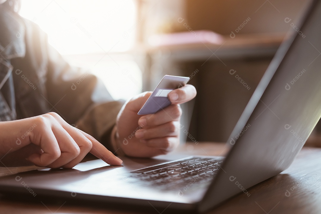 Mãos segurando um cartão de crédito e usando um laptop.