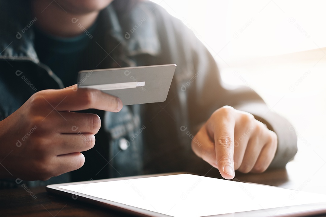 Mãos segurando um cartão de crédito e usando um laptop.