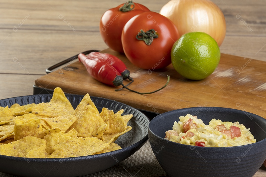 Guacamole com tortilhas com ingredientes ao fundo