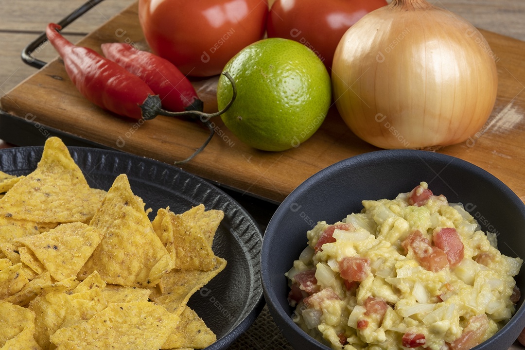 Guacamole com tortilhas com ingredientes ao fundo
