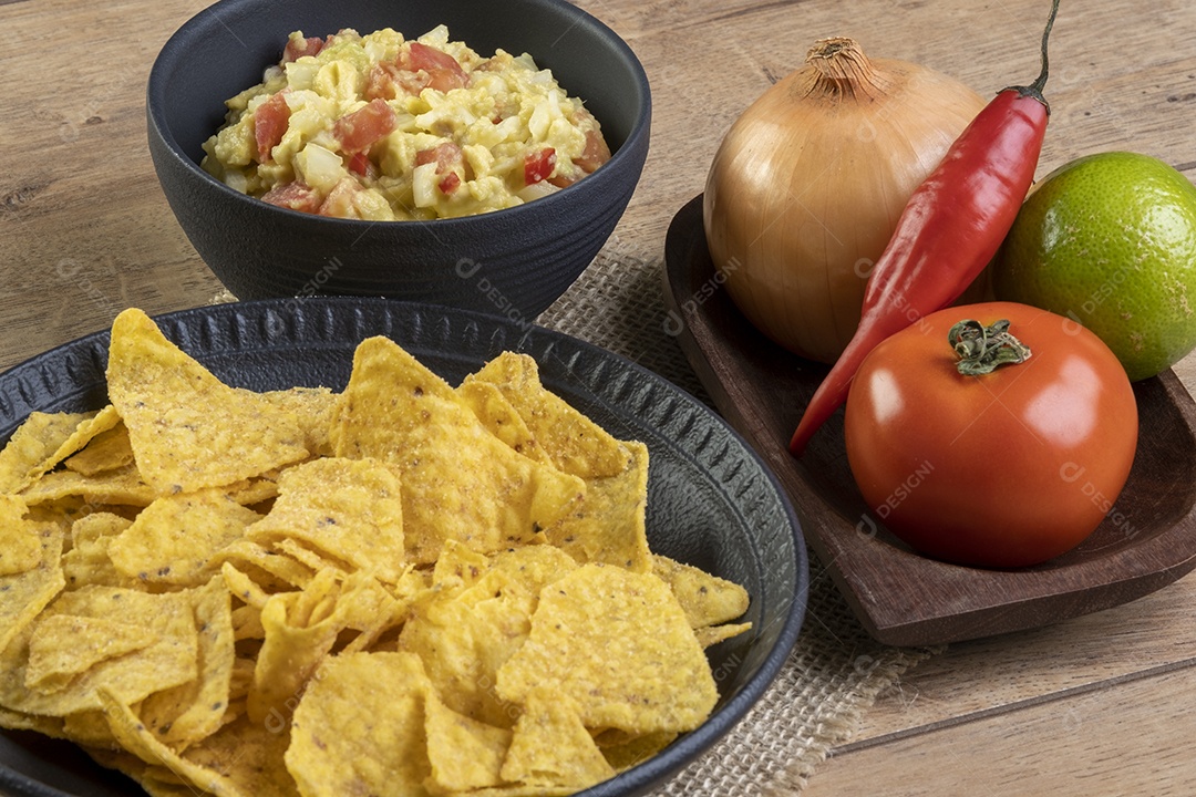 Guacamole com tortilhas com ingredientes ao fundo