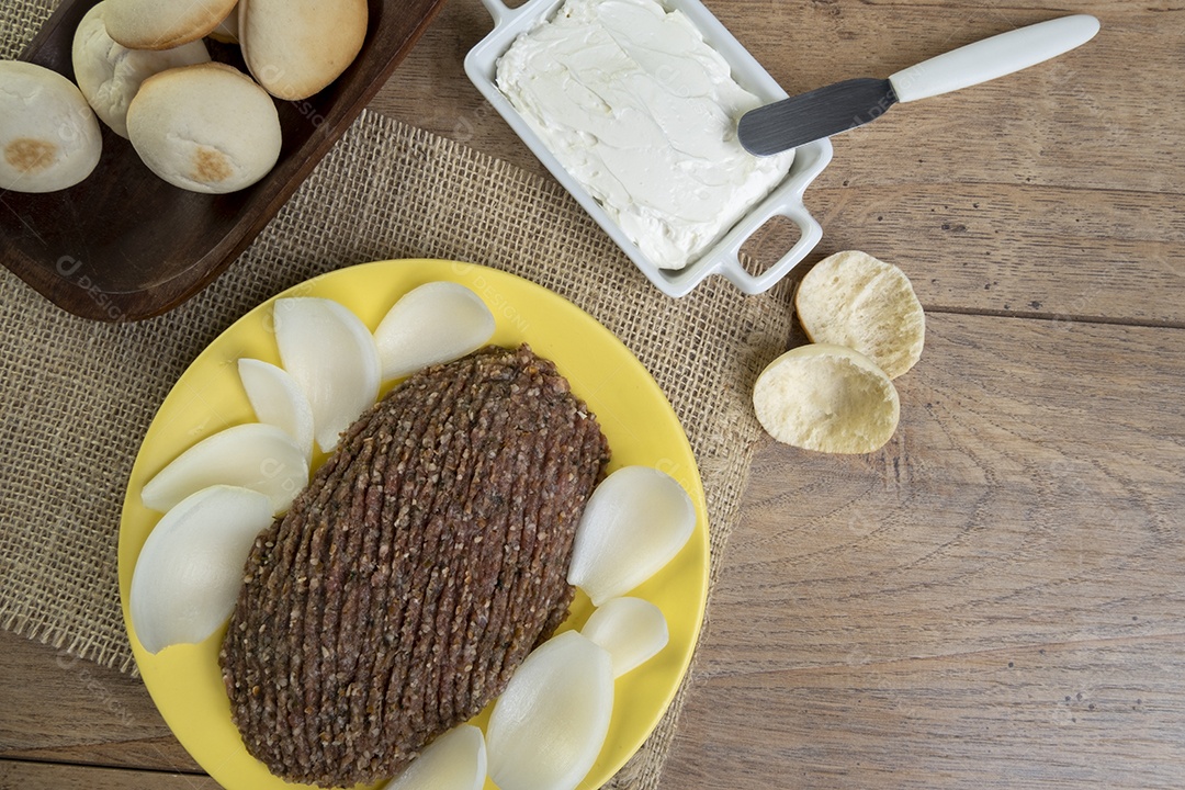 Quibe cru com cebola fatiada, requeijão, pão pita e folhas de hortelã.