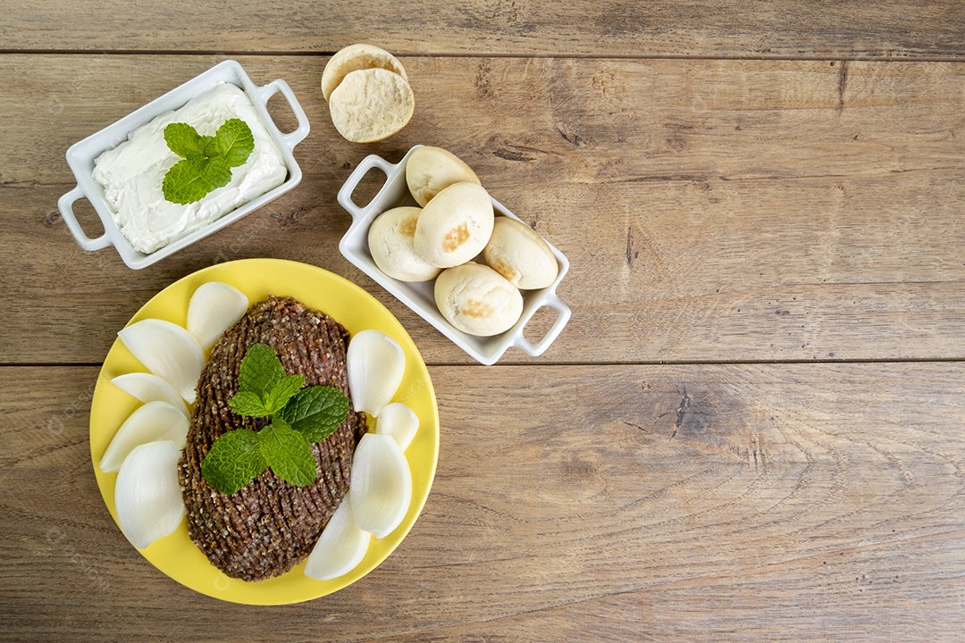 Quibe cru com cebola fatiada, requeijão, pão pita e folhas de hortelã.