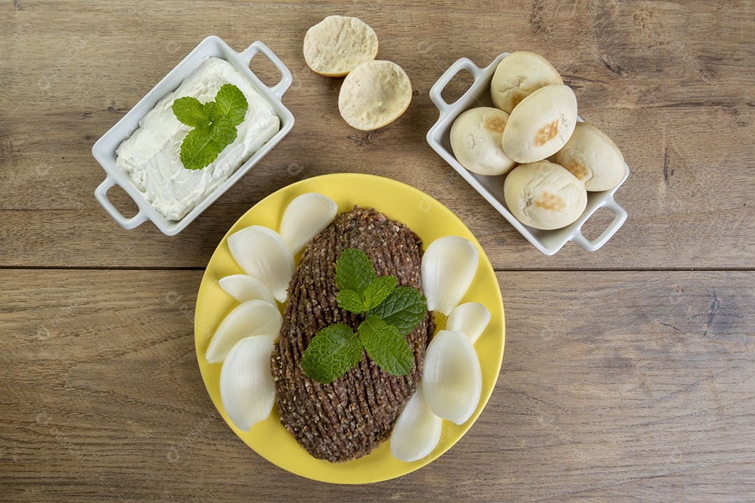 Quibe cru com cebola fatiada, requeijão, pão pita e folhas de hortelã.