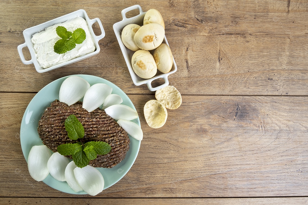 Quibe cru com cebola fatiada, requeijão, pão pita e folhas de hortelã.