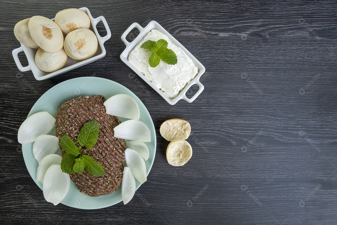 Quibe cru com cebola fatiada, requeijão, pão pita e folhas de hortelã.