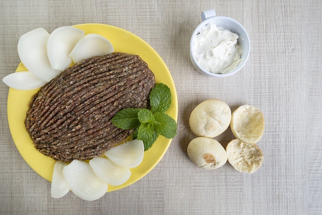 Quibe cru com cebola fatiada, requeijão seco, pão sírio e folha de hortelã