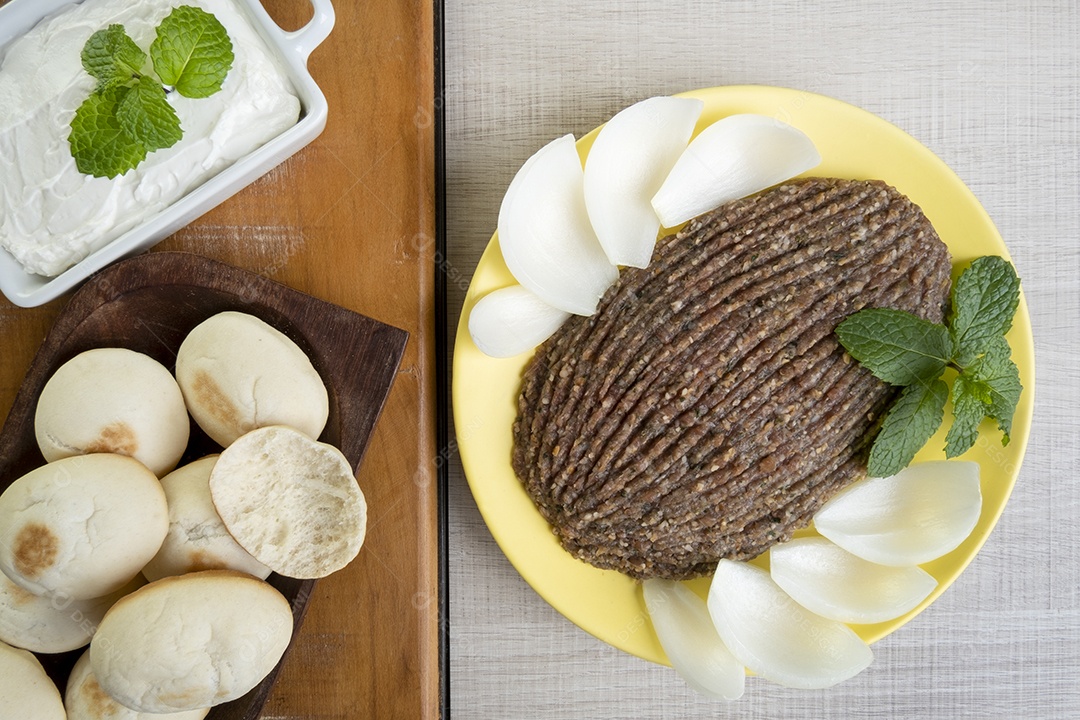 Quibe cru com cebola fatiada, requeijão, pão pita e folhas de hortelã.