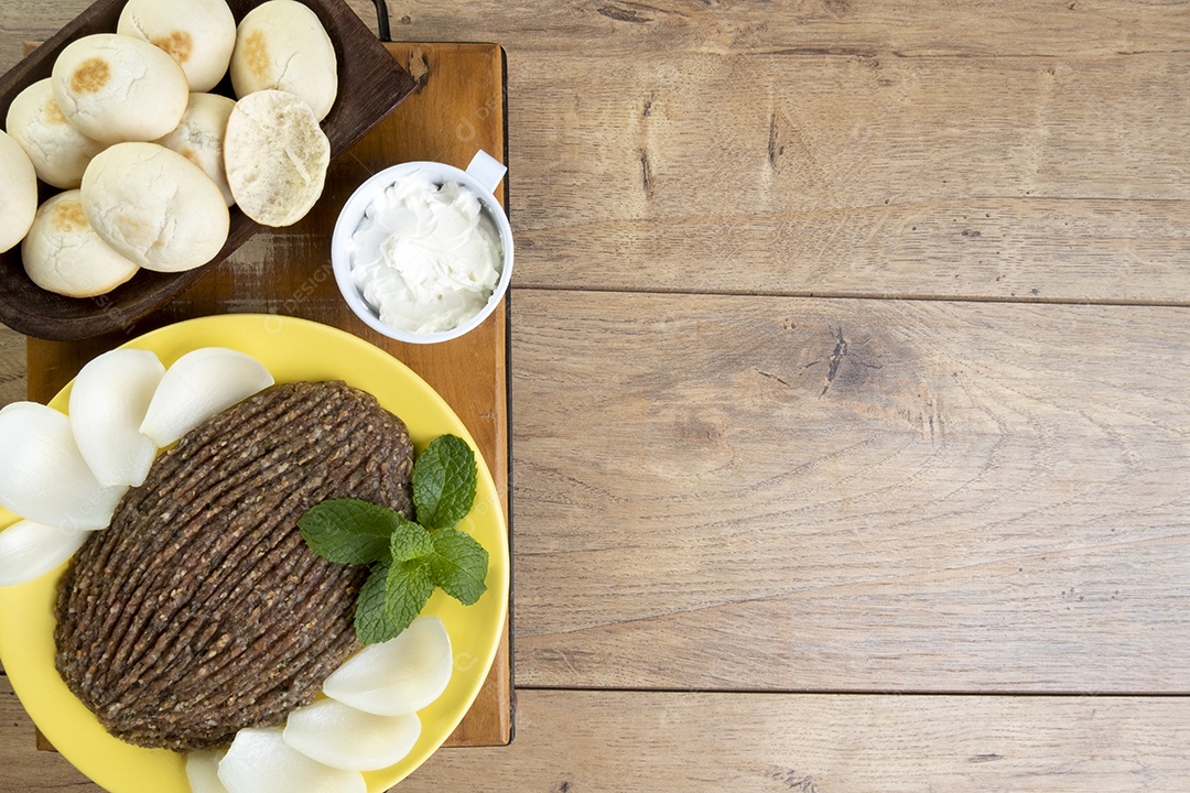 Quibe cru com cebola fatiada, requeijão, pão pita e folhas de hortelã.