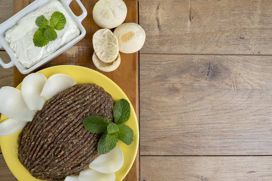Quibe cru com cebola fatiada, requeijão, pão pita e folhas de hortelã.