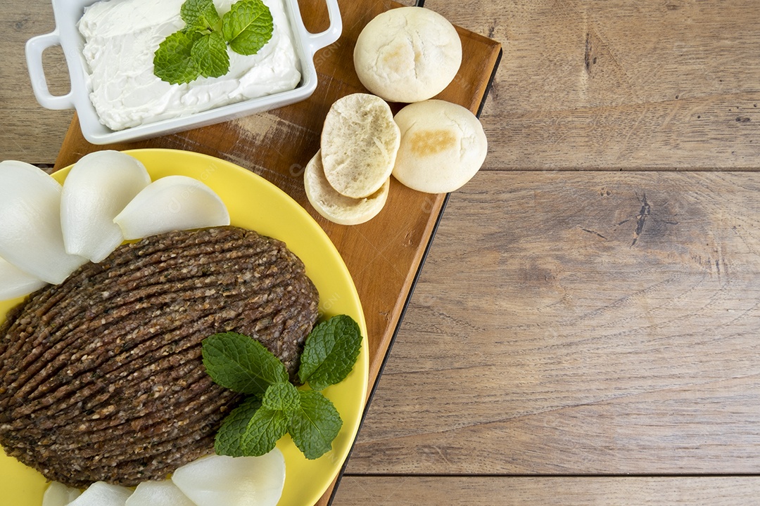 Quibe cru com cebola fatiada, requeijão, pão pita e folhas de hortelã.
