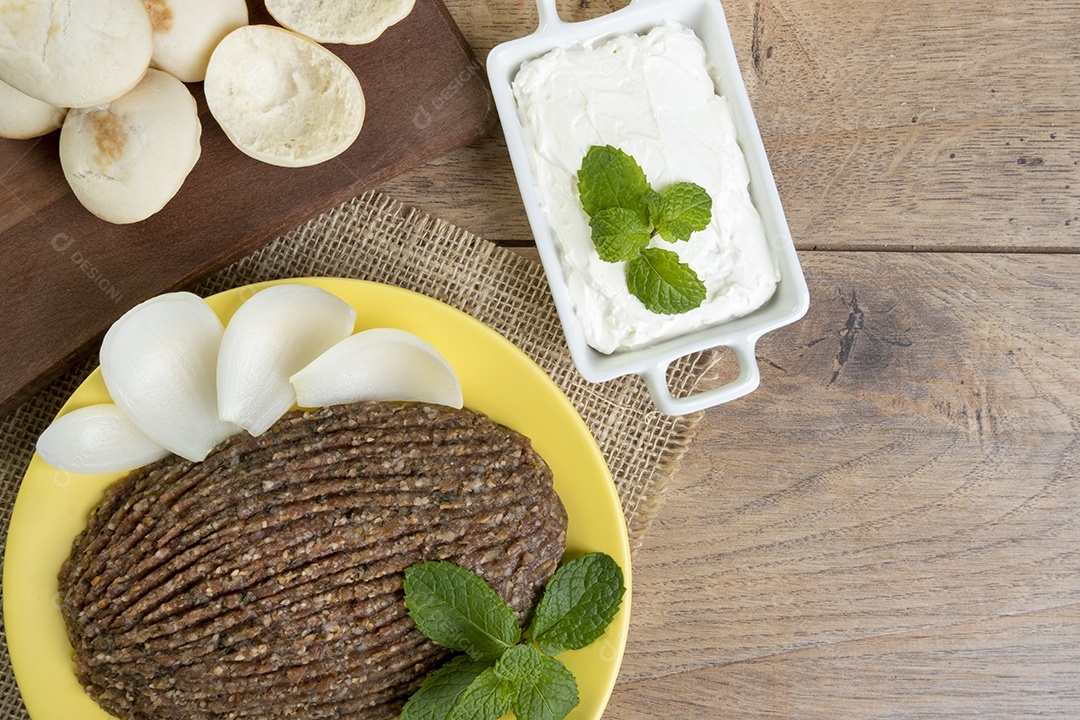 Quibe cru com cebola fatiada, requeijão, pão pita e folhas de hortelã.