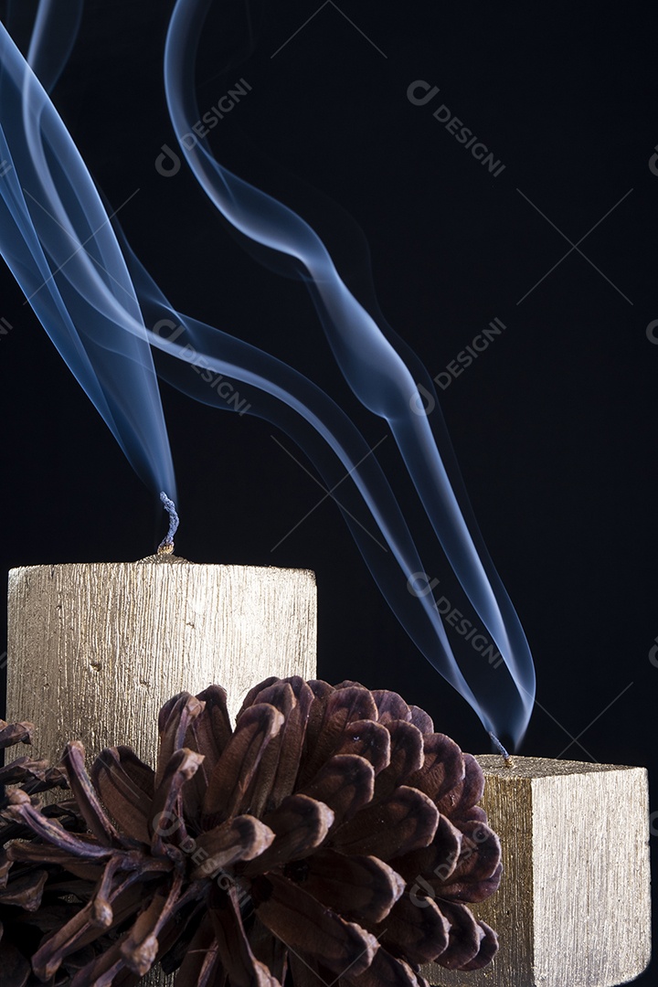 Duas velas douradas apagadas com pinhas ao redor no escuro