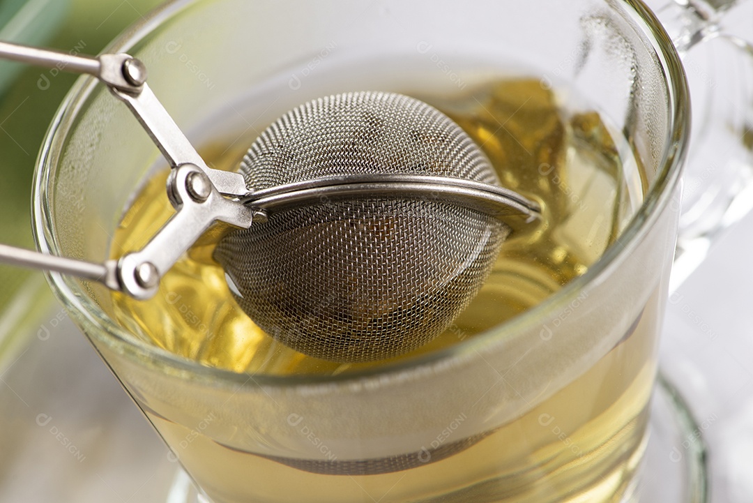 Closeup de um infusor com chá em um copo com água quente