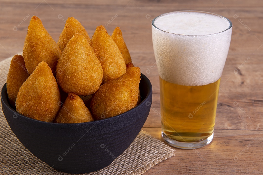 Tradicional petisco brasileiro frito feito com frango conhecido como coxinha e um copo de cerveja.