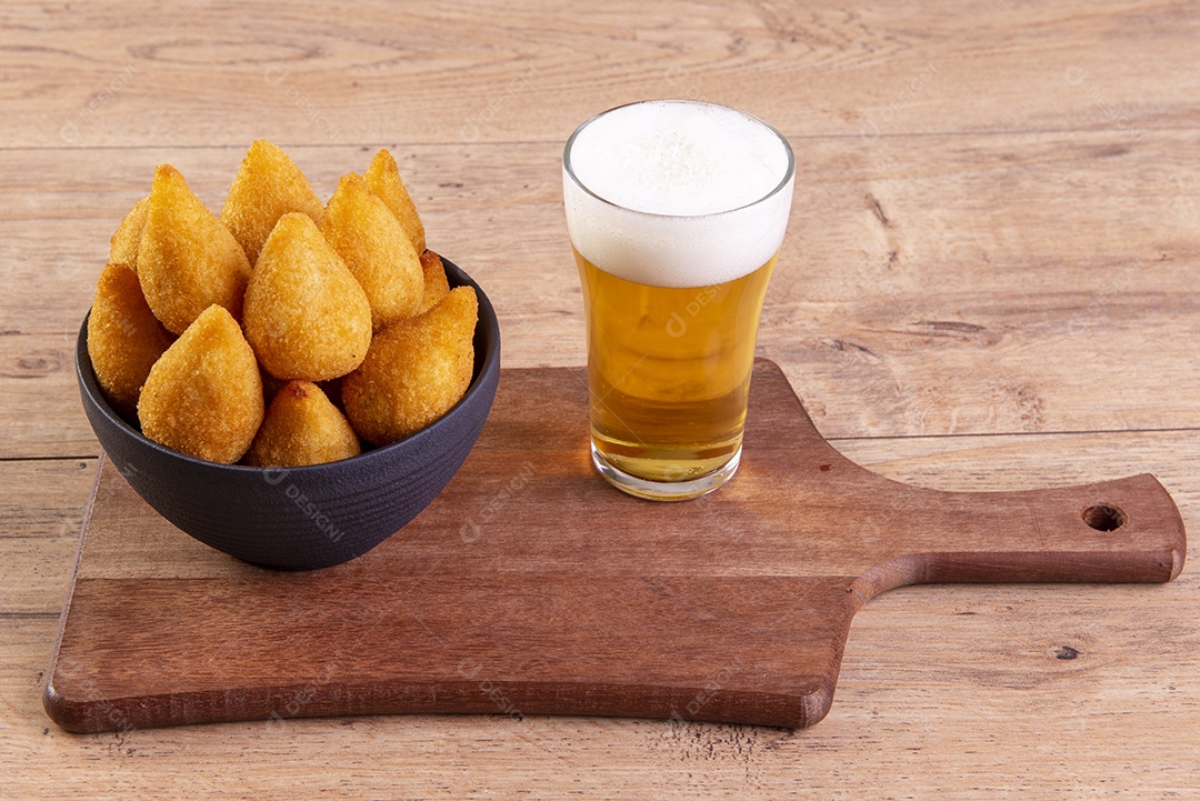 Tradicional petisco brasileiro frito feito com frango conhecido como coxinha e um copo de cerveja.