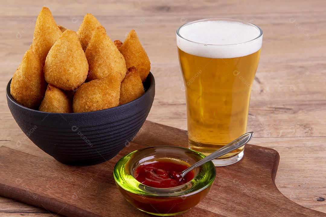 Tradicional petisco brasileiro frito feito com frango conhecido como coxinha e um copo de cerveja.