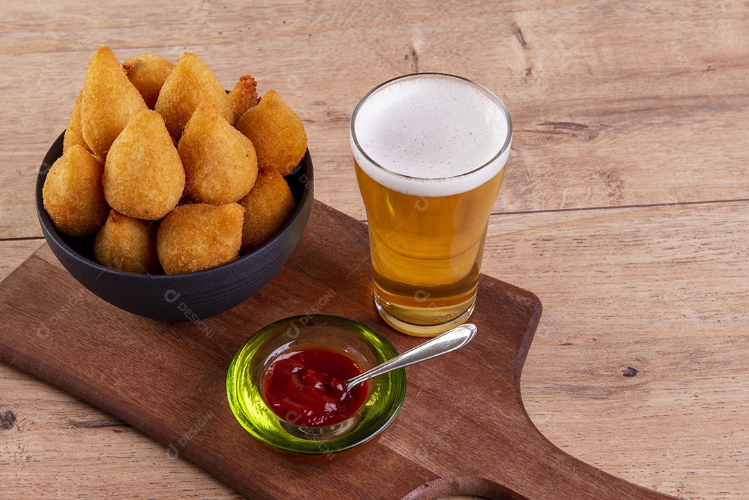 Tradicional petisco brasileiro frito feito com frango conhecido como coxinha e um copo de cerveja.