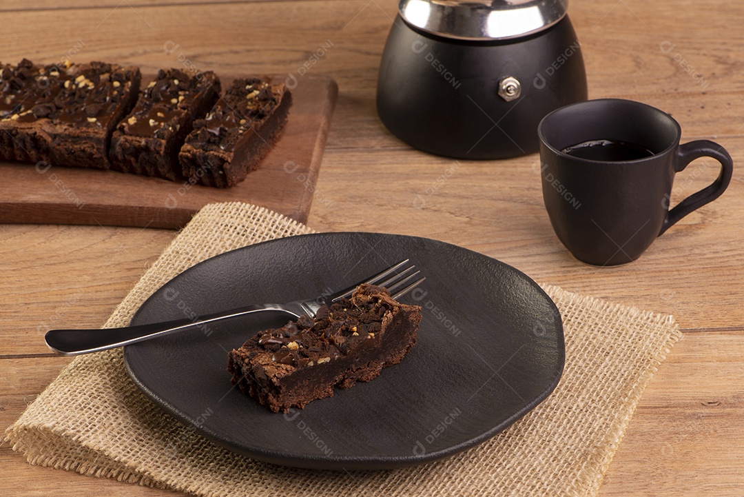 Uma fatia de brownie em um prato com uma xícara de café na mesa de madeira.