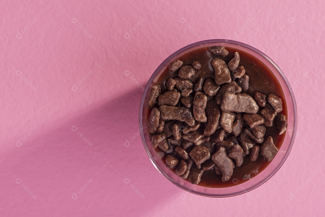 Copo de acrílico com brigadeiro e granulado de chocolate no fundo rosa