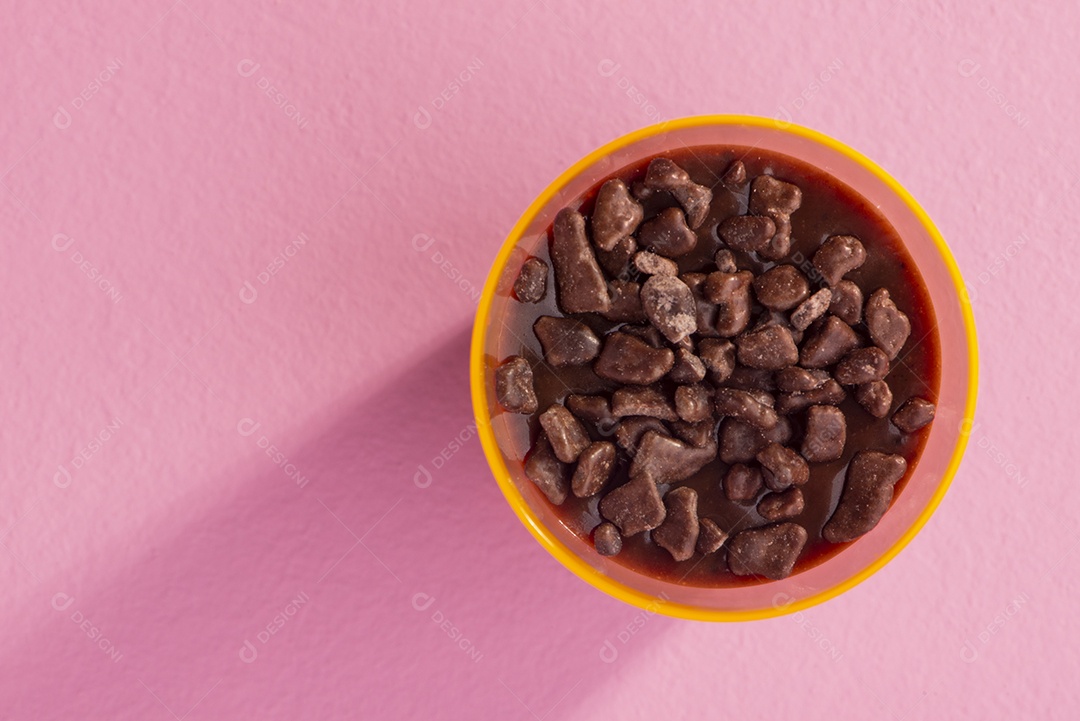 Copo de acrílico com brigadeiro e granulado de chocolate no fundo rosa