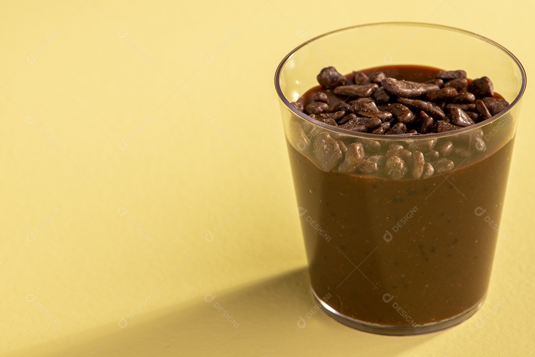 Copo de acrílico com brigadeiro e granulado de chocolate no fundo rosa