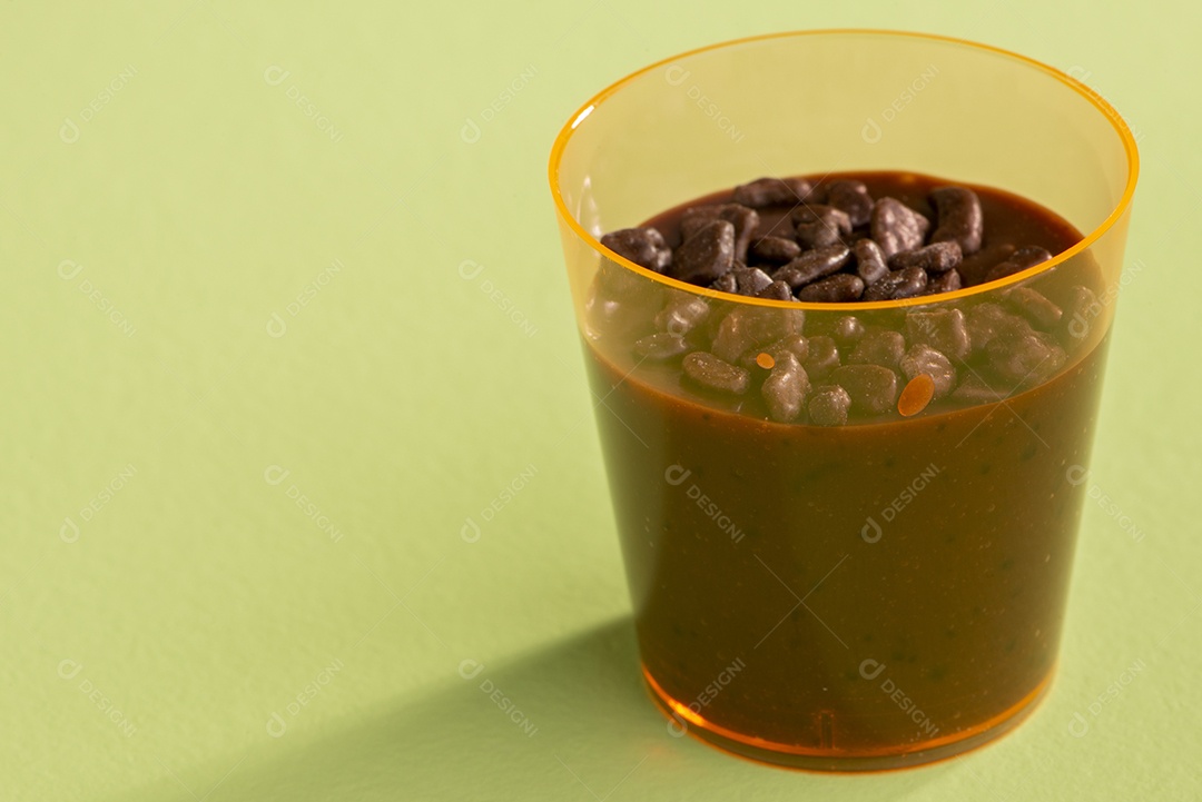 Copo de acrílico com brigadeiro e granulado de chocolate no fundo rosa