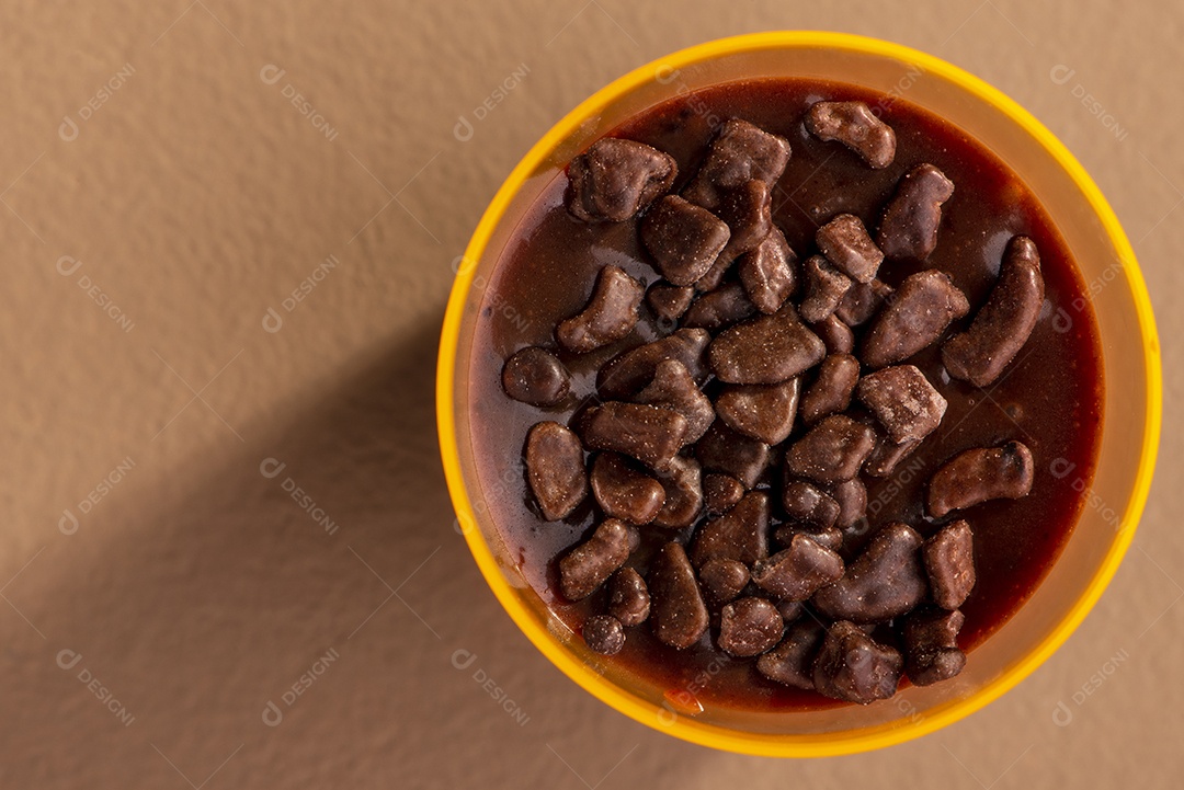 Copo de acrílico com brigadeiro e granulado de chocolate no fundo rosa