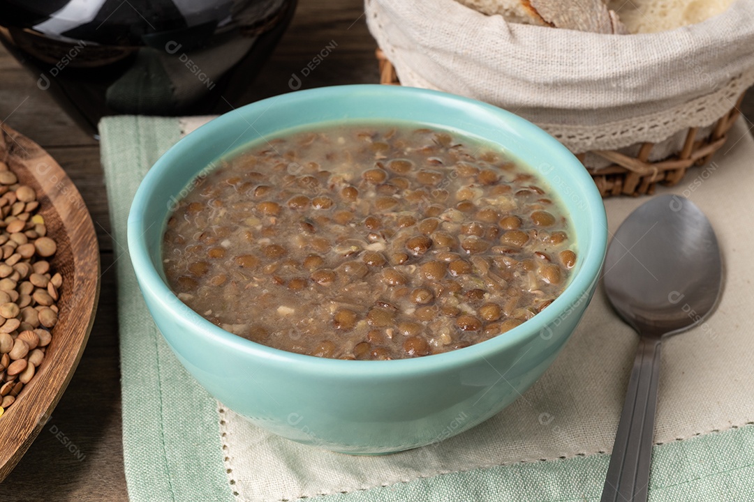 Sopa de lentilha marrom em uma tigela com fatias de pão e vinho sobre madeira