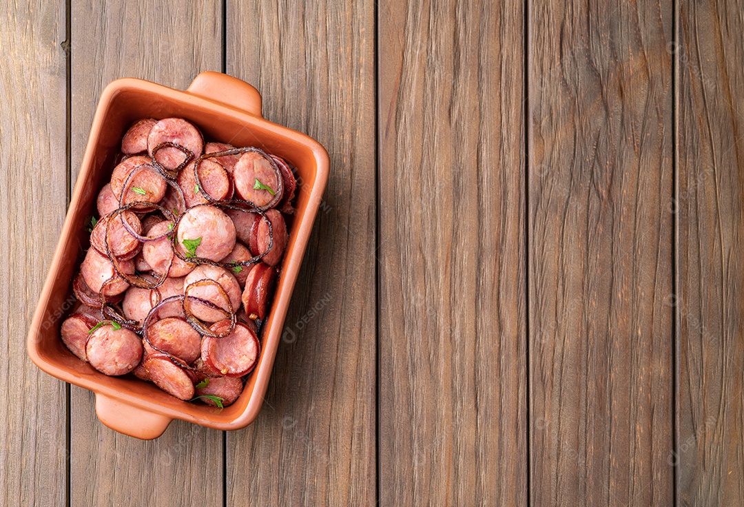 Porção de linguiça calabresa grelhada com cebola sobre mesa de madeira