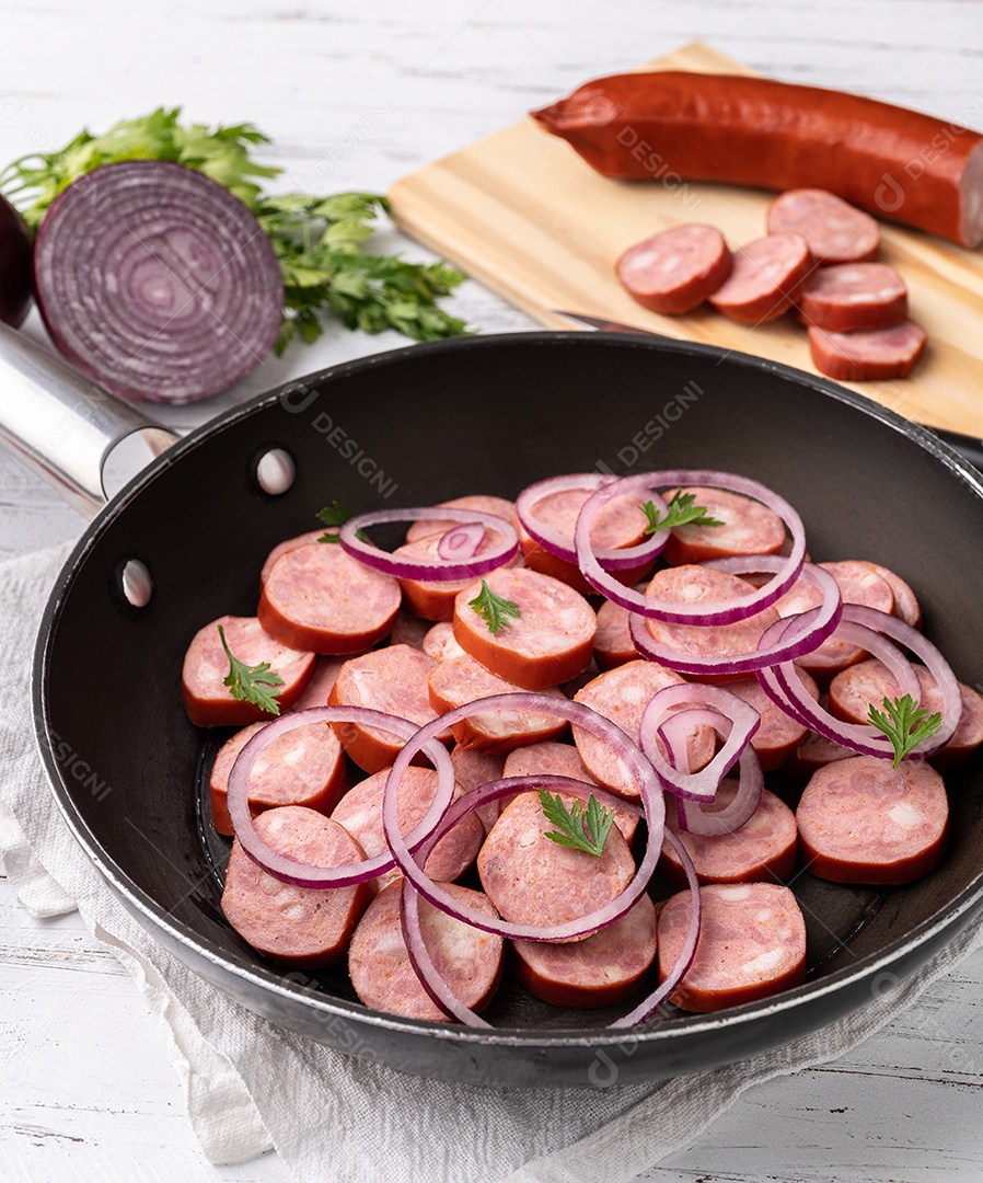 Fatias de linguiça calabresa crua em uma panela com cebola, pimenta