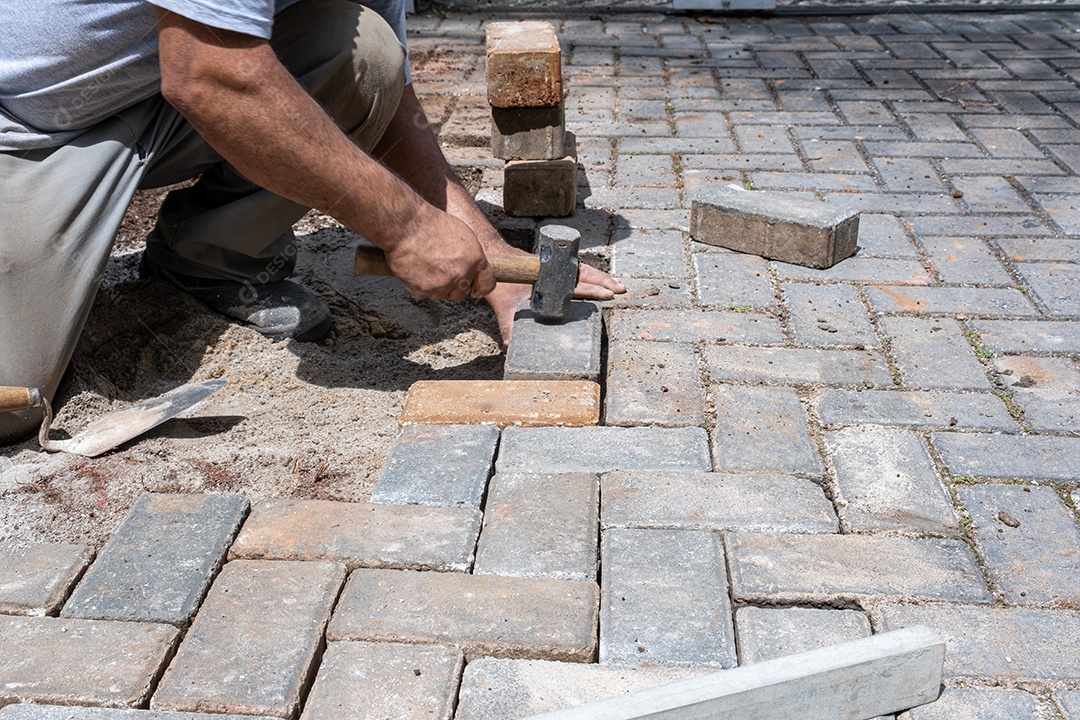 Brasileiro e trabalhador da construção civil batendo um pequeno martelo no bloco de concreto.