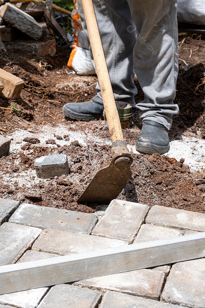 Brasileiro usando uma enxada para preparar o solo para assentamento de blocos de concreto
